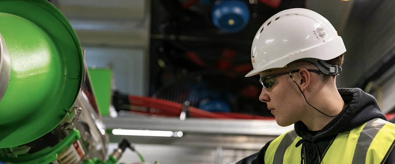 Technician wearing a hard hat and safety glasses beside industrial pipework.